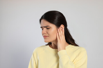 Canvas Print - Young woman suffering from ear pain on light grey background