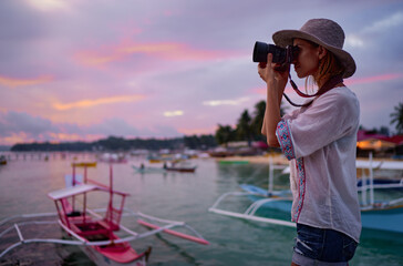Wall Mural - Photography and travel. Young woman in hat holding camera  with beautiful tropical sea view.