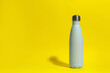 Stylish light blue thermo bottle with water drops on yellow background, space for text