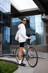 Sticker - African american woman in sunglasses and cycling shorts standing near bike on street 