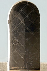 Poster - one black old iron door with a wrought iron pattern on a white stone wall in the street