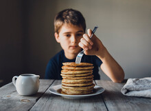Close Up Of A Boy Sticking A Fork Into A Big Stack Of Pancakes.