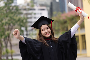 Successful graduation from university. Smiling beautiful Asian girl university or college graduate showing with diploma over university at background.