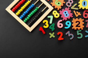 Many colorful numbers and mathematical symbols near abacus on black background, flat lay. Space for text