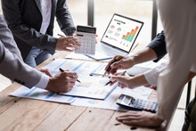 Group Of Confident Business People Point To Graphs And Charts To Analyze Market Data, Balance Sheet, Account, Net Profit To Plan New Sales Strategies To Increase Production Capacity.	