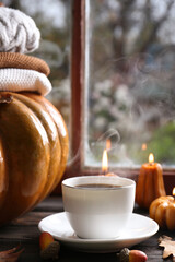 Wall Mural - Cup of hot drink and pumpkin shaped candles on wooden table near window. Cozy autumn atmosphere