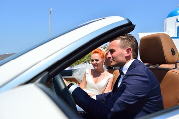 Wall Mural - Beautiful young couple bride and groom posing in the white car on Santorini island, Greece