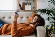 © Westend61 - Happy young man using smart phone relaxing on sofa at home