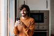 © Westend61 - Happy young man using smart phone in kitchen at home