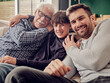 © Westend61 - Happy grandfather, father and son sitting together on couch in living room