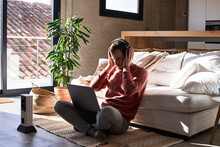 Man Wearing Headphones Sitting With Laptop On Rug At Home