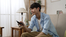 impatient asian Japanese man shaking head with dissatisfied look on face while channel surfing with a tv controller on the couch in the living room at home