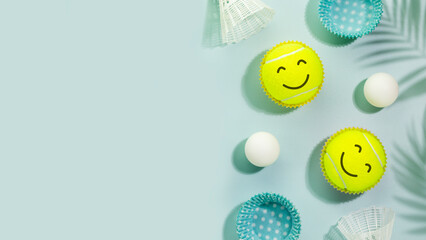 Summer sport activities and healthy lifestyle with tennis balls with smile faces, table tennis balls and shuttlecocks on blue background with palm shadows.. Tennis, table tennis, badminton. Copy space