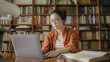 © Synthex - Asian woman student working on laptop, researching information at library archives