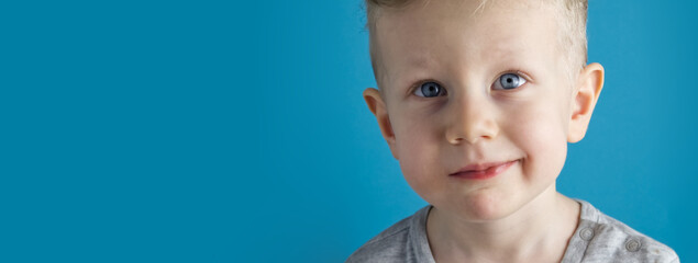 Portrait of a blue-eyed and fair-haired toddler boy on a blue background close-up