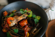 Close up shot of a bowl of large prawns with mussels topped with green leaves and tomatoes