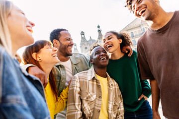 Happy group of Multiracial young friends having fun in city street. United millennial people hugging each other laughing together outdoors. Community and friendship concept