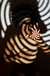 © VISTA by Westend61 - Spiral pattern shadow on woman in front of wall
