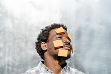 Contemplative Man With Yellow Adhesive Notes On Face In Front Of Wall