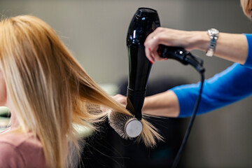 Close up of a hair stylist using hairdryer and a brush for hair styling.