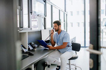 Young multiracial doctor sitting at reception and calling.