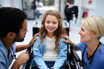 Wall Mural - young multiracial doctor with his colleague talking with little girl on wheelchair.