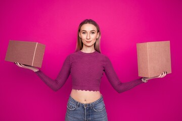 A young woman holds two cardboard boxes on a pink background