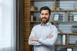© Liubomir - Portrait of successful businessman in office, man in shirt smiling and looking at camera, mature boss with beard with shaggy hands standing at workplace inside building.