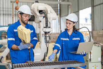 Male and female engineer training using remote controller control robot arm welding machine in industrial factory. Team of technician automation robot in uniform explains robot arm system.