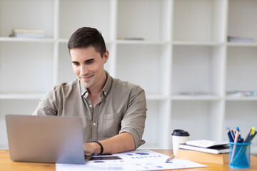 Handsome young businessman in office working on laptop and financial documents analyzing and planning financial accounts.