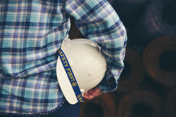 Wall Mural - Construction Engineer and safety and health Officer concept. Man Hand engineer holding safety hat (helmet). Safety Officer inspector in front of construction site with metal roll background.