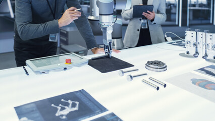 Fototapete - Modern Robotic Arm Holding and Moving a Mechanical Metal Component. Diverse Team of Engineers Using Tablet Computer to Manipulate and Program the Robot.