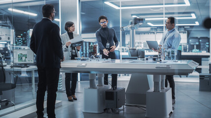 Leinwandbilder - Diverse Team of Industrial Robotics Engineers Gathered Around a Table With Robotic Arm. Scientists Use Laptop Computer to Manipulate and Program the Robot to Pick Up and Move a Powerful Microchip.