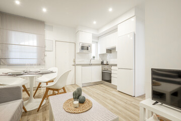 Wall Mural - Studio apartment with an open plan kitchen with white cabinets and a round white dining table with resin chairs