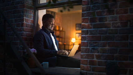Poster - African American Uses Laptop While Sitting on Windowsill in a Brooklyn Style Brownstone House at Night. Black Male Writer Thinking about his Novel's Story and Working on his Next Book Project