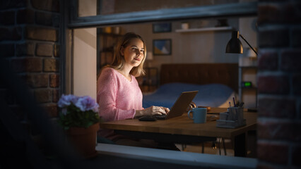 Poster - Working from Home Concept: Creative Female Designer Using Laptop, Thinking and Creating New Visual Concept for Online Marketing Campaign. Night Shot, Viewed Through a Window from Outside