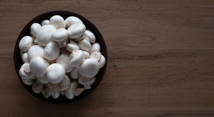 Wall Mural - Fresh white mushrooms in a bowl on a wooden table top view.