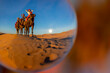 Three Riders And Their Handler Travel Through The Saharan Desert On Their Camels In Morocco