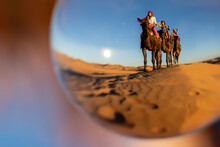 Three Riders And Their Handler Travel Through The Saharan Desert On Their Camels In Morocco