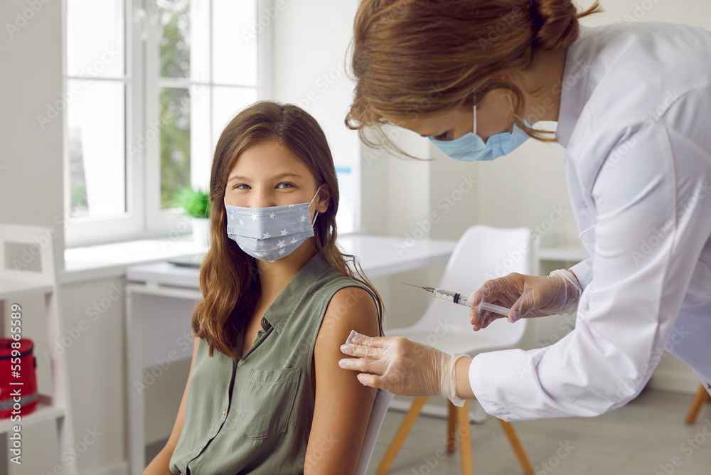 Vaccination of children. Smiling child in protective mask receiving vaccine shot against covid infection at vaccination center. Female nurse in medical mask makes injection in hand of preteen girl.
