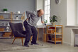 © Studio Romantic - Upset senior man suffering from lower back pain. Elderly man getting up from chair using cane at home. Pensioner having injury and needing rehabilitation. Healthcare and medical concept
