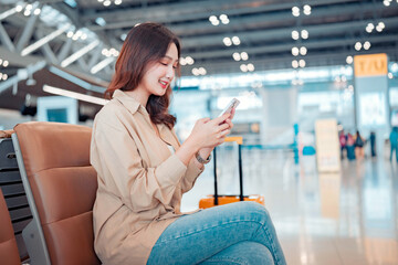 Happy asian tourist woman passenger using mobile smartphone with suitcase traveling between waits for flight in Airport Terminal, Browse Internet, flight check in, Tourist journey trip concept