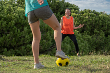 Two 30s years old woman training to play soccer or European football in amateur team. Yellow ball, sport field with green grass.