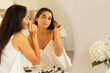 Young beautiful woman with long straight dark hair and fresh clean skin doing morning makeup routine, using eye liner in front of mirror table at home. Beauty and facial cosmetics concept