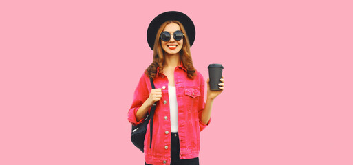 Portrait of stylish modern smiling young woman with cup of coffee wearing jacket, black round hat on pink background