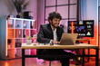 © Sofiia Shunkina - Portrait of handsome experienced smart stylish curly bearded manager, businessman, wearing suit sitting at table, using laptop at evening time in modern office.