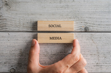 Male hand stacking two wooden pegs with a Social media sign on them