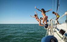 Multiracial Friends Jumping Out Of Boat In The Sea While Having Fun In Their Summer Vacation - Luxury Travel Concept
