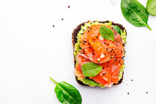 Avocado Salmon Sandwich Or Toast On Rye Bread With Spinach, Crushed Cashew Nuts And Sesame Seeds, White Table Background, Top View