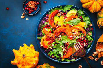 Fresh pumpkin salad with lettuce,  red cabbage, avocado, arugula, pomegranate seeds and nuts. Healthy vegan vegetarian eating, slow comfort food. Blue table background. Top view